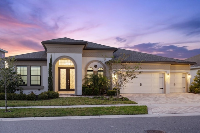 view of front of property with decorative driveway, french doors, roof with shingles, stucco siding, and a garage