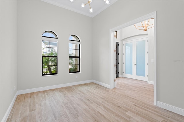 empty room featuring baseboards, ornamental molding, an inviting chandelier, french doors, and light wood-type flooring