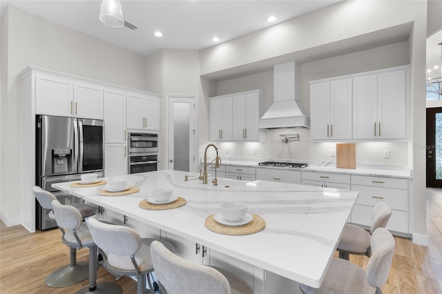 kitchen featuring light wood-style flooring, stainless steel appliances, premium range hood, a sink, and white cabinetry