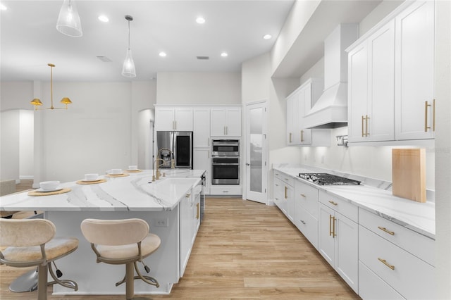 kitchen with light wood-style flooring, white cabinetry, hanging light fixtures, appliances with stainless steel finishes, and custom range hood