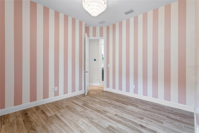 spare room with a notable chandelier, wood finished floors, visible vents, baseboards, and wallpapered walls