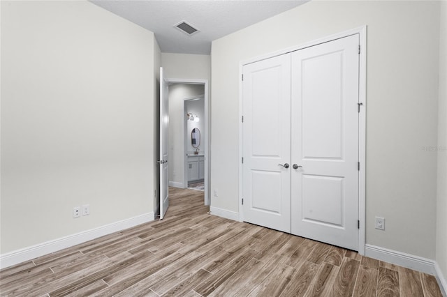 unfurnished bedroom featuring a closet, visible vents, light wood-style floors, a textured ceiling, and baseboards