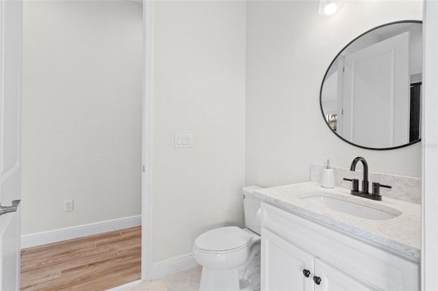 half bath featuring baseboards, vanity, toilet, and wood finished floors