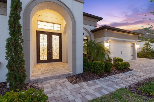 view of exterior entry with an attached garage, driveway, french doors, and stucco siding