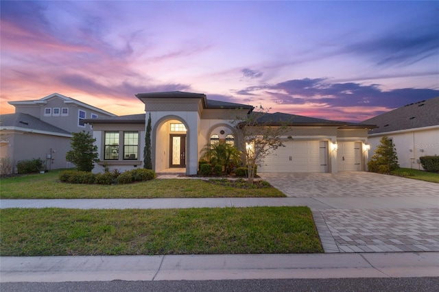 mediterranean / spanish-style home with an attached garage, stucco siding, decorative driveway, and a yard