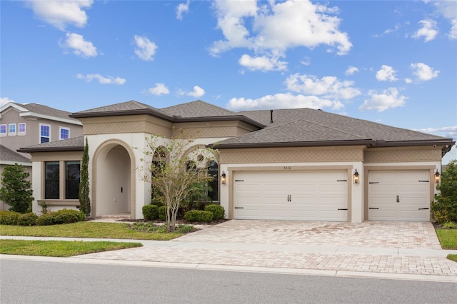 view of front of property with a garage, a shingled roof, decorative driveway, and stucco siding