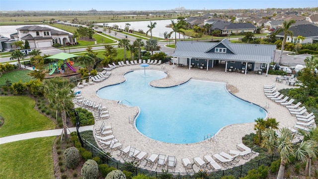 community pool with a water view, a lawn, a patio area, fence, and a residential view