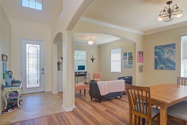 foyer entrance featuring light wood finished floors, baseboards, arched walkways, ornamental molding, and an inviting chandelier