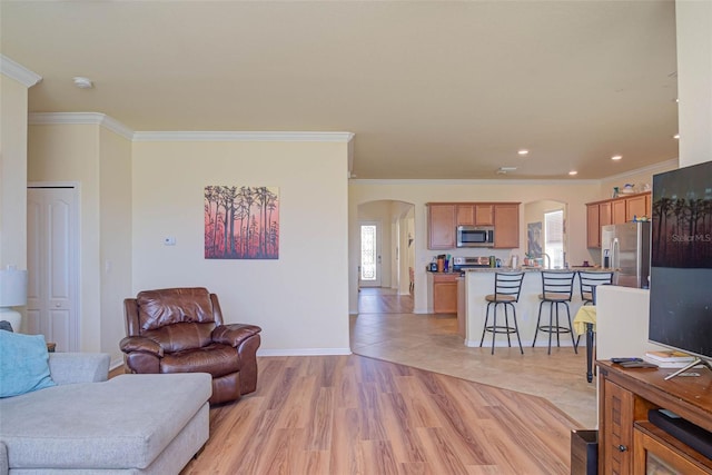 living area with arched walkways, light wood-style flooring, a wealth of natural light, and crown molding