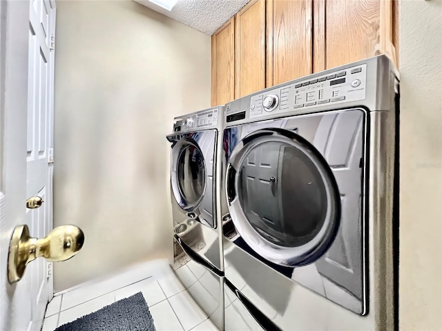 clothes washing area with light tile patterned floors, a textured ceiling, cabinet space, and washer and dryer