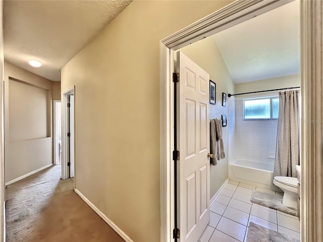 hallway with tile patterned flooring, a textured ceiling, and baseboards