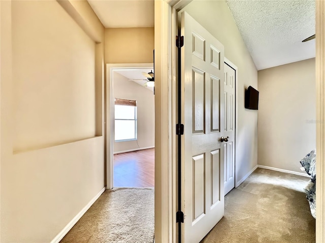 corridor featuring carpet, baseboards, and a textured ceiling