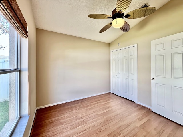 unfurnished bedroom featuring lofted ceiling, a closet, a textured ceiling, and light wood finished floors