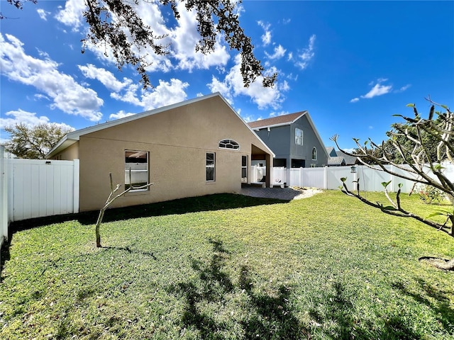 back of house with a patio area, a fenced backyard, a yard, and stucco siding