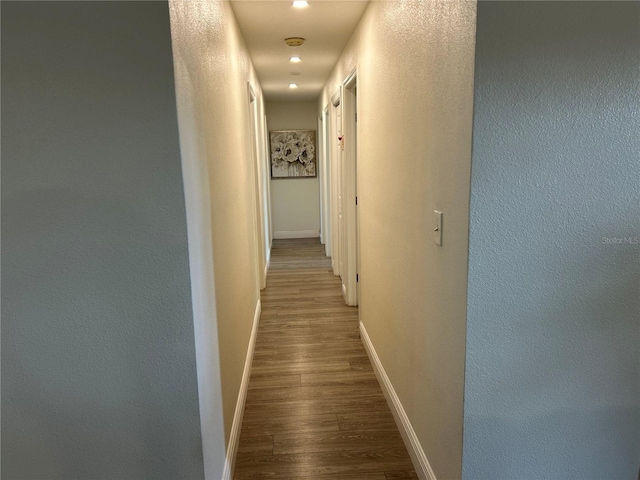 hall with a textured wall, baseboards, and wood finished floors