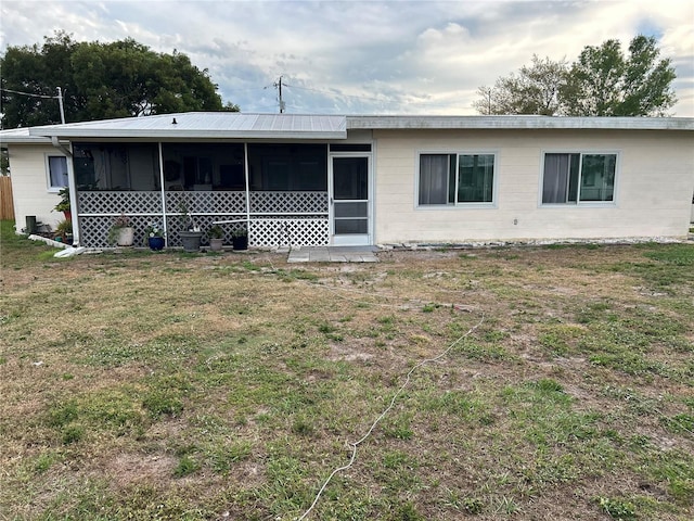 back of house with a sunroom, a yard, and concrete block siding