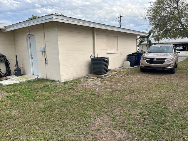 view of home's exterior with concrete block siding, central AC, and a lawn