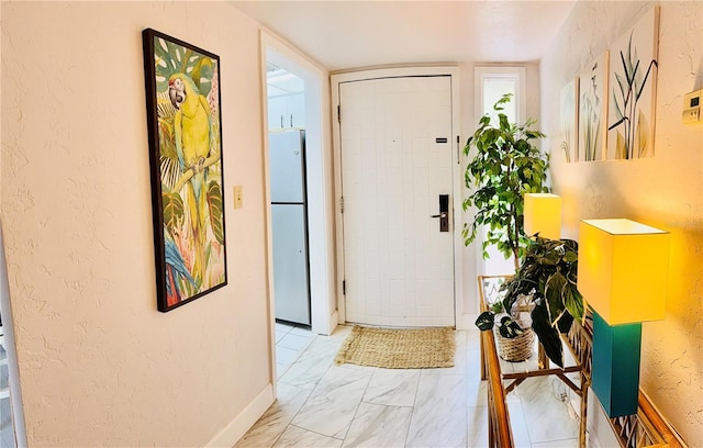 foyer featuring marble finish floor, baseboards, and a textured wall