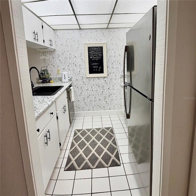 kitchen with a drop ceiling, light tile patterned floors, stainless steel appliances, white cabinetry, and a sink