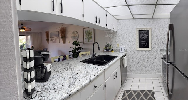 kitchen featuring wallpapered walls, a drop ceiling, freestanding refrigerator, light tile patterned flooring, and a sink