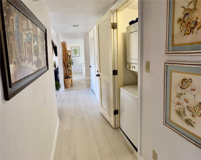 hallway featuring light wood-type flooring, stacked washer and clothes dryer, and a textured wall