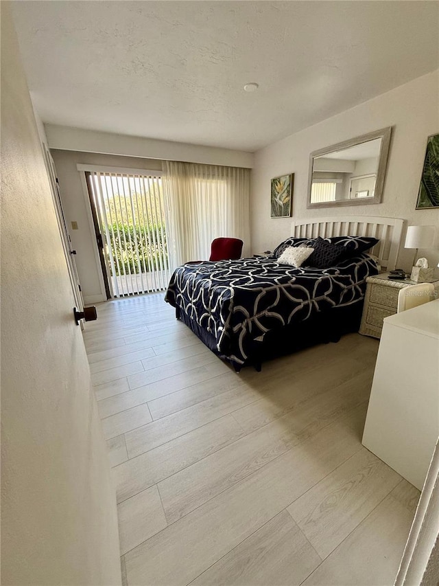 bedroom with access to exterior, a textured ceiling, and wood finished floors