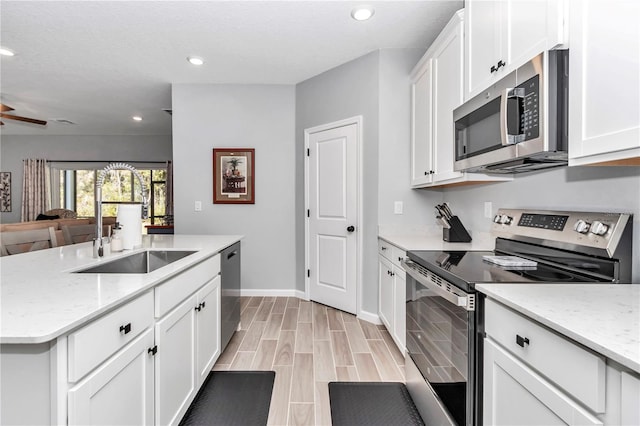 kitchen with a kitchen island with sink, recessed lighting, wood finish floors, white cabinets, and appliances with stainless steel finishes