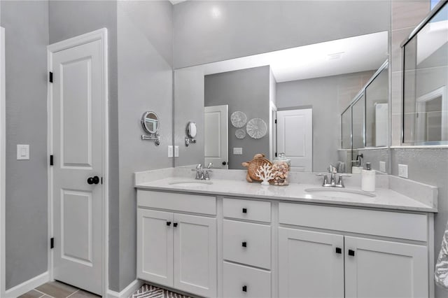 full bath with a sink, a shower stall, baseboards, and double vanity