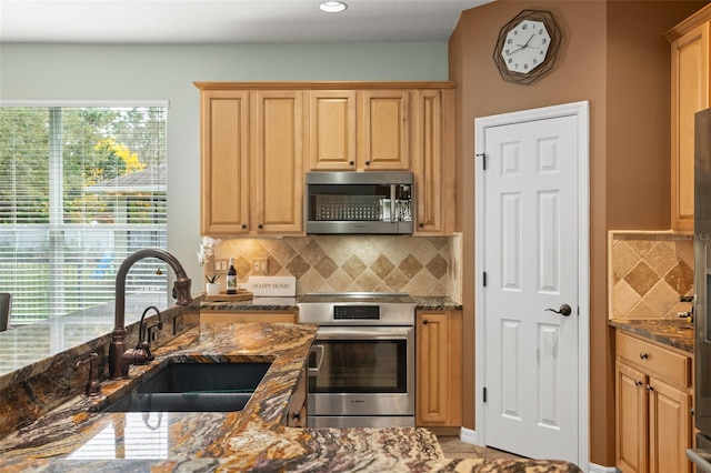 kitchen with appliances with stainless steel finishes, dark stone counters, a sink, and decorative backsplash