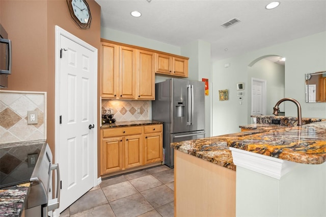 kitchen with tasteful backsplash, arched walkways, dark stone counters, stainless steel fridge with ice dispenser, and light tile patterned flooring