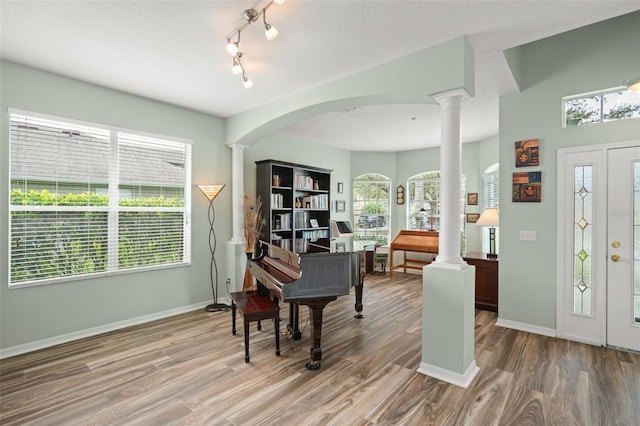 office space with baseboards, decorative columns, arched walkways, and wood finished floors