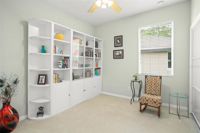 living area with a ceiling fan, light carpet, and baseboards