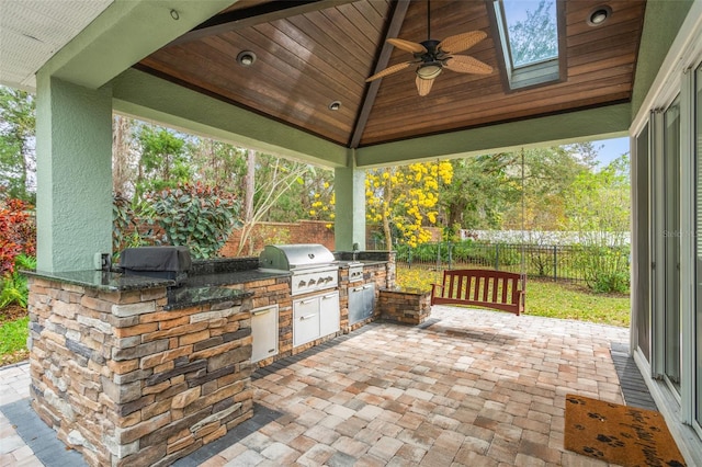 view of patio featuring a ceiling fan, area for grilling, fence, exterior kitchen, and a gazebo