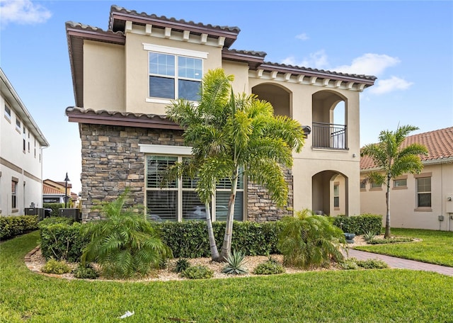 mediterranean / spanish-style house with stone siding, a balcony, a front lawn, and stucco siding