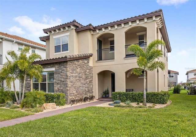 mediterranean / spanish-style home featuring stone siding, a front lawn, a balcony, and stucco siding