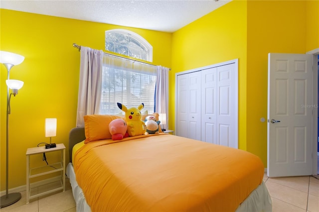 bedroom featuring a closet, a textured ceiling, baseboards, and light tile patterned floors