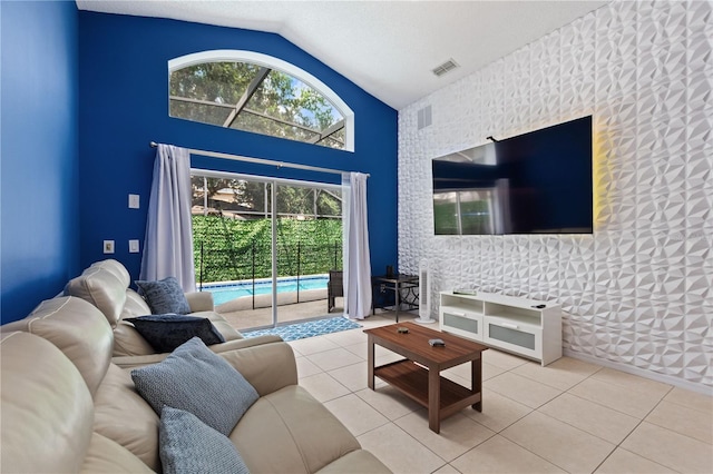 living area with high vaulted ceiling, an accent wall, visible vents, and tile patterned floors