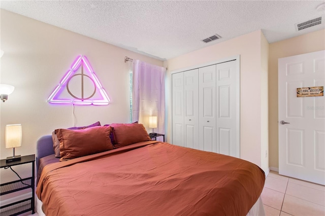 bedroom featuring light tile patterned floors, a closet, a textured ceiling, and visible vents