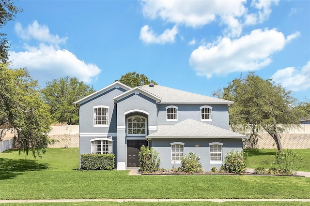 view of front of home with stucco siding, roof with shingles, fence, and a front yard