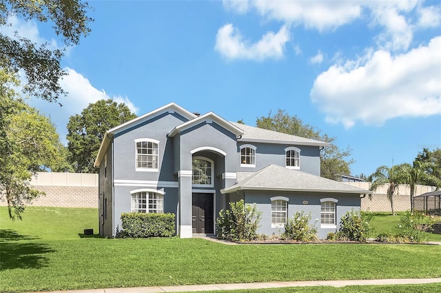 view of front of property featuring a front lawn, roof with shingles, fence, and stucco siding