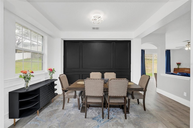 dining room with arched walkways, light wood-type flooring, plenty of natural light, and visible vents