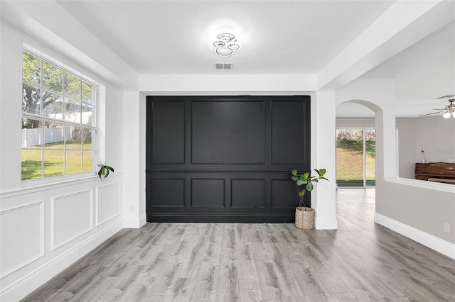 foyer entrance with baseboards, visible vents, arched walkways, light wood-style floors, and a decorative wall