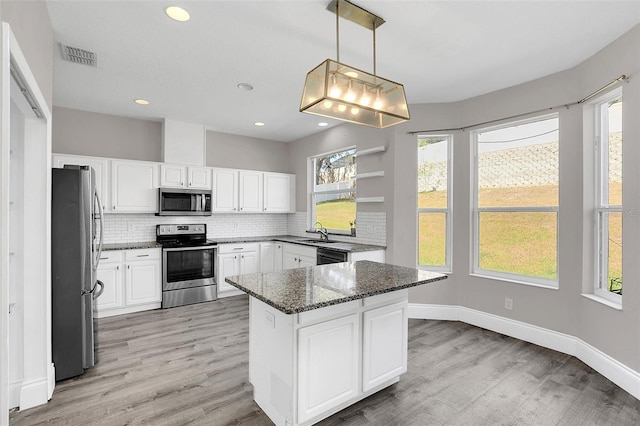 kitchen featuring stainless steel appliances, light wood-style flooring, decorative backsplash, a sink, and dark stone countertops