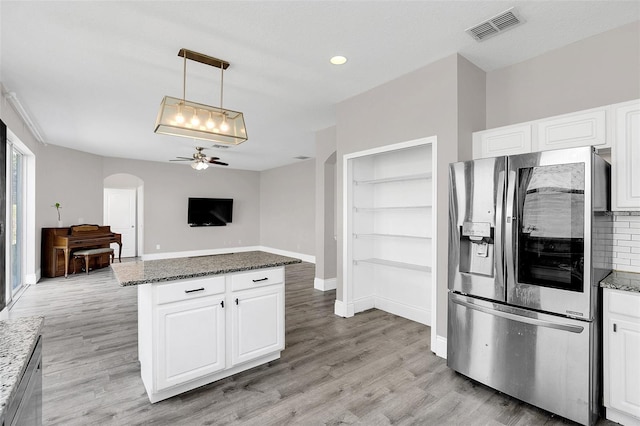 kitchen with arched walkways, stainless steel refrigerator with ice dispenser, visible vents, white cabinetry, and light wood-type flooring