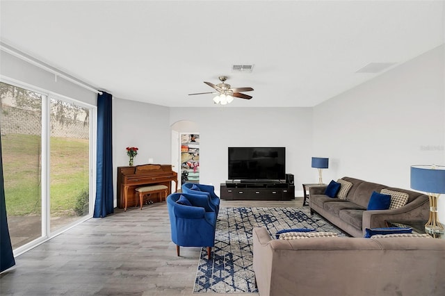 living room with arched walkways, wood finished floors, visible vents, and a ceiling fan