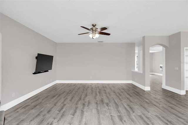 unfurnished living room with baseboards, visible vents, a ceiling fan, arched walkways, and wood finished floors