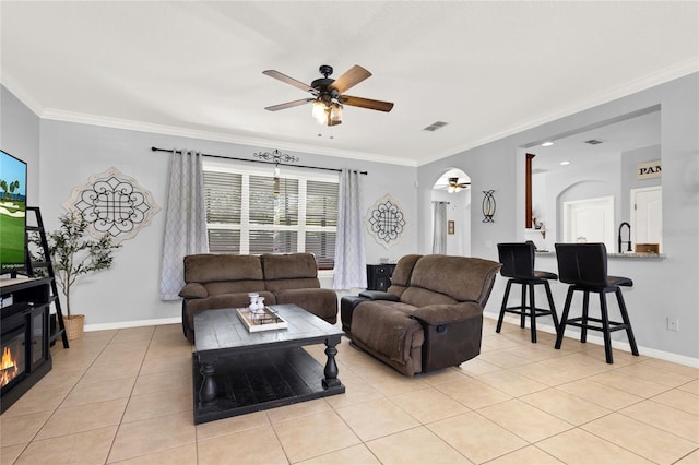 living area featuring light tile patterned floors, ceiling fan, visible vents, baseboards, and ornamental molding