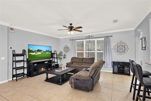 living room with light tile patterned floors, ceiling fan, ornamental molding, and a glass covered fireplace