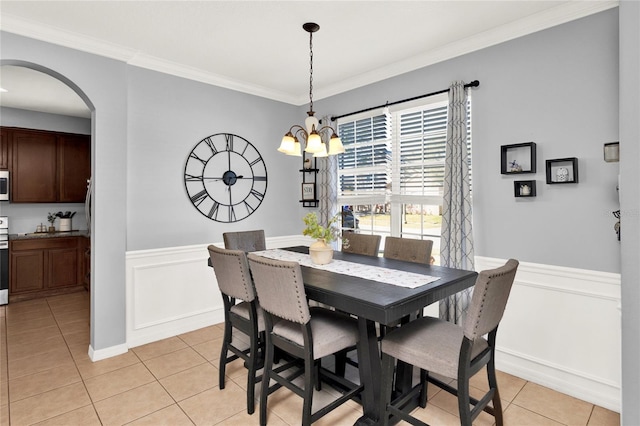 dining area featuring light tile patterned floors, arched walkways, ornamental molding, and wainscoting