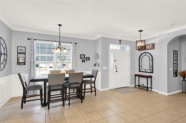 dining space with arched walkways, ornamental molding, light tile patterned flooring, and an inviting chandelier